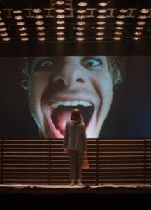 A white man's head is on a big screen.