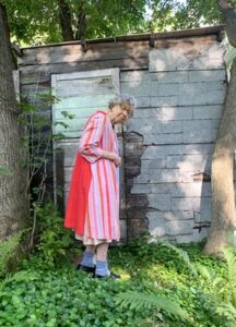 A old white woman wears a patterned red and white dress as she poses
