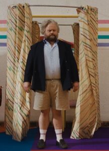 A white man stands wearing shorts