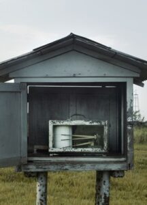 A gray tree house on stilts on top of a field