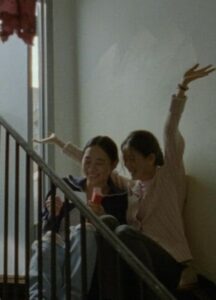 Two women sit in front of a stairway.